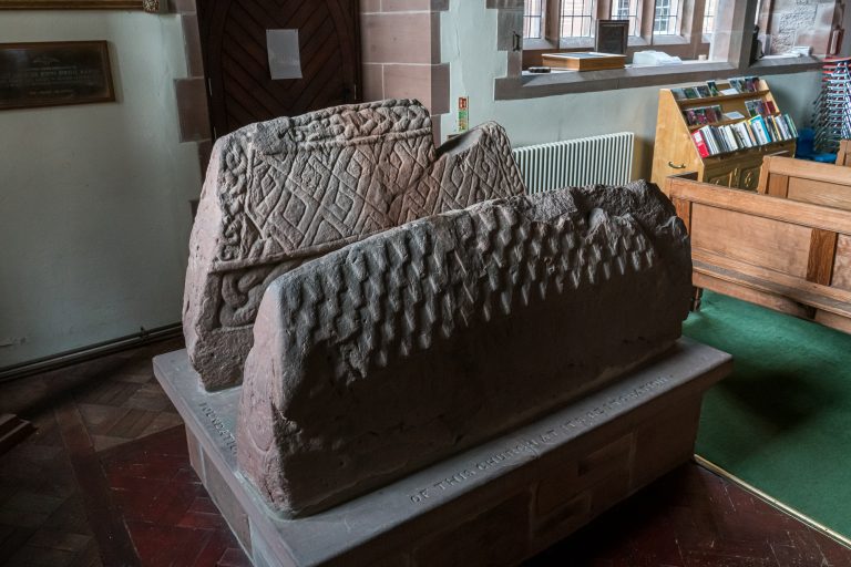 Two carved Viking Age hogback tombstones shaped like longhouses with shingled roofs, inside St Mary’s Church, Gosforth, Cumbria