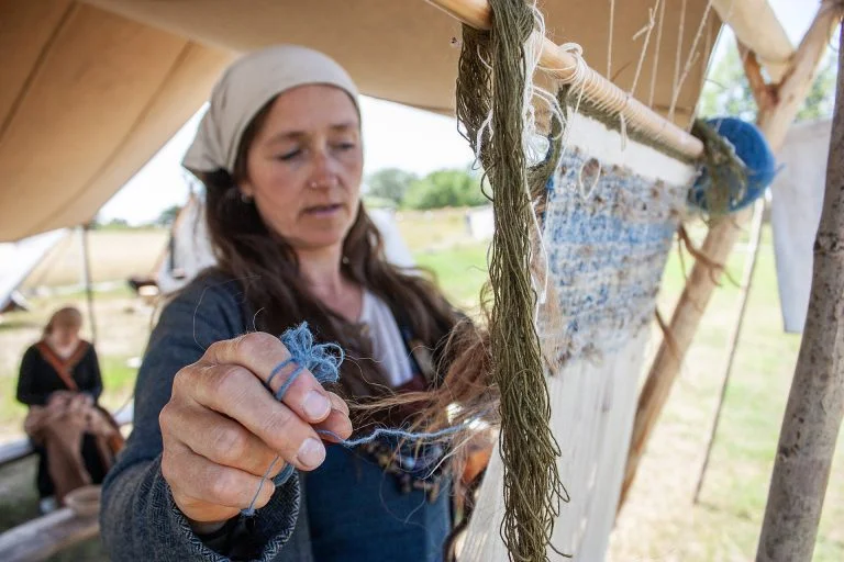 A volunteer weaving on an upright loom at a reconstructed Viking village, one way to get involved in living history