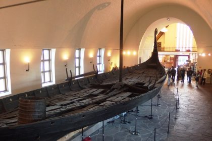 The Oseberg ship on its supports in the long white hall of the old Viking Ship Museum in Oslo, its curled prow rising toward the arched ceiling