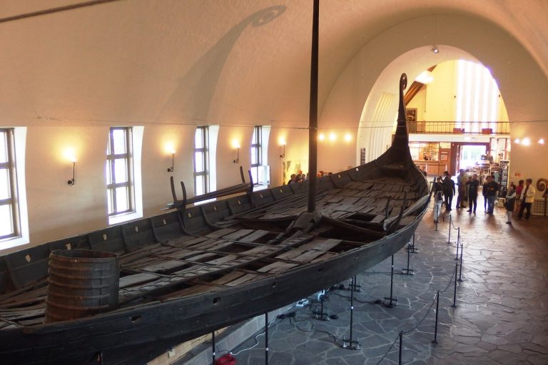 The Oseberg ship on its supports in the long white hall of the old Viking Ship Museum in Oslo, its curled prow rising toward the arched ceiling
