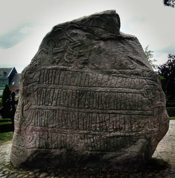 The larger Jelling runestone, its broad face carved with lines of runes, standing on a cobbled square in Jelling, Denmark